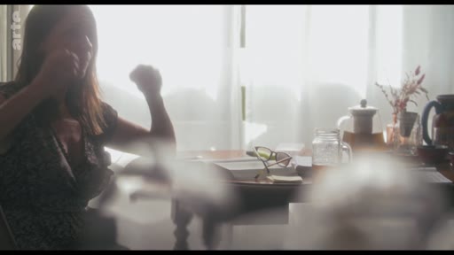 Une femme est filmée en contre-jour lors d'une interview, assise à une table avec des objets personnels, dans le cadre d'une discussion sur la création de personnage.