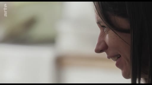 Une femme est filmée en gros plan de profil alors qu'elle sourit pendant une discussion ou un entretien.