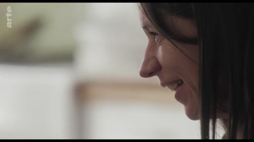 Gros plan sur le visage d'une femme souriante, capturé lors d'un entretien filmé dans un cadre intimiste.