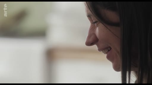 Gros plan sur le visage d'une femme souriante, capturé lors d'une séquence de tournage ou d'interview.