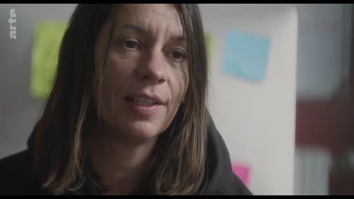 Une femme est filmée en gros plan lors d'une interview, s'exprimant face caméra dans un cadre informel avec des notes adhésives colorées en arrière-plan.