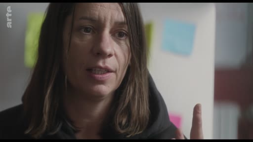 Une femme s'exprime face caméra lors d'une interview, avec des post-its colorés visibles en arrière-plan.