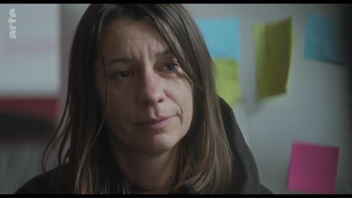 Une femme, probablement une actrice, est filmée en gros plan lors d'une discussion sur le plateau de tournage, avec des post-its colorés visibles en arrière-plan.