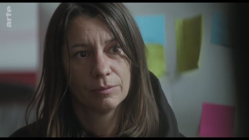 Gros plan sur une femme lors d'une discussion, probablement une actrice ou une réalisatrice, dans un cadre de travail avec des post-its colorés en arrière-plan.