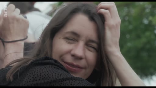 Portrait d'une femme souriante, les cheveux au vent, lors d'un moment de détente en extérieur.