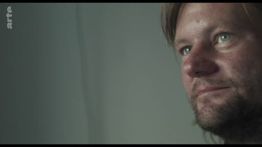 Un homme observe avec attention des images sur un écran, dans une séquence évoquant le visionnage de vieilles cassettes vidéo.