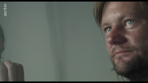 Un homme regarde une vidéo sur un écran, capturé en gros plan. L'image provient d'une archive télévisuelle de la chaîne Arte.