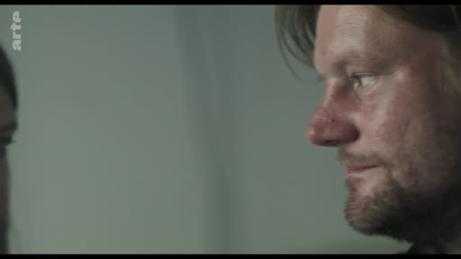 Un homme observe attentivement une vidéo diffusée sur un écran, dans le cadre d'une séquence d'archives. Le logo de la chaîne Arte est visible dans le coin supérieur gauche de l'image.