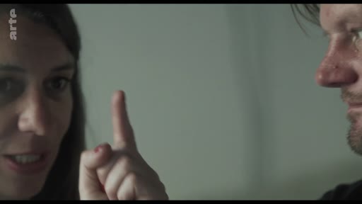 Une femme, vue en gros plan, lève l'index pour faire une mise en garde ou un avertissement lors d'une discussion avec un homme. La scène semble extraite d'une archive vidéo ou d'un film.
