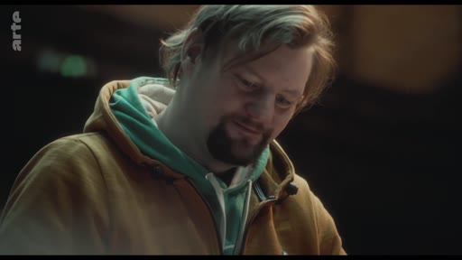 Un homme portant un sweat-shirt à capuche jaune et vert exprime sa vulnérabilité lors d'un moment de réflexion intense.