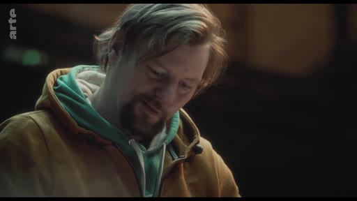 Un homme d'âge moyen, portant un sweat-shirt à capuche, affiche une expression de vulnérabilité et de réflexion dans ce gros plan.