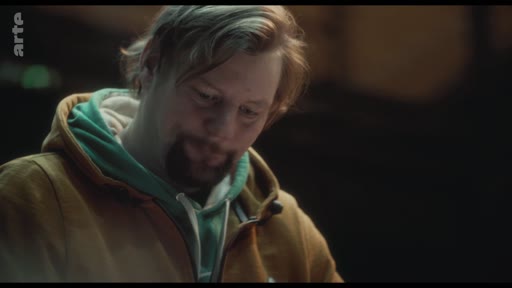 Un homme avec une barbe et une veste à capuche exprime sa vulnérabilité et ses émotions dans un moment de réflexion intense.