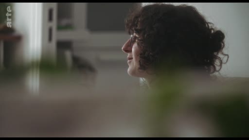 Une femme aux cheveux bouclés, vue de profil, participe à une discussion dans un cadre intérieur. L'image est capturée lors d'un échange, probablement dans le cadre d'une interview ou d'un entretien.