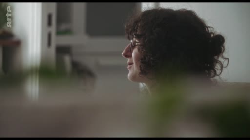 Une femme aux cheveux bouclés, vue de profil, participe à une discussion dans un cadre intérieur. L'image est capturée lors d'un échange sur un roman.