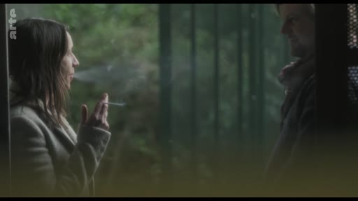 Une femme fume une cigarette tout en ayant une conversation avec un homme dans un cadre extérieur, possiblement près d'une plage.