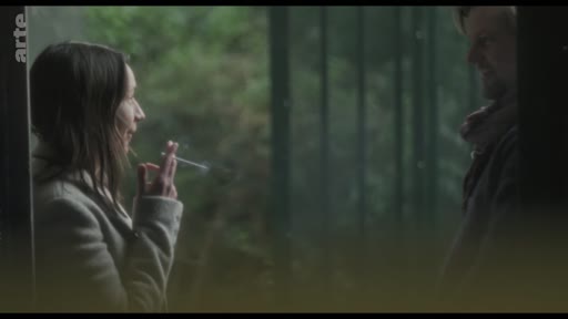 Une femme et un homme se font face dans un espace extérieur, la femme tient une cigarette à la main. Cette scène illustre une interaction intime ou une discussion entre deux personnages dans un cadre naturel.
