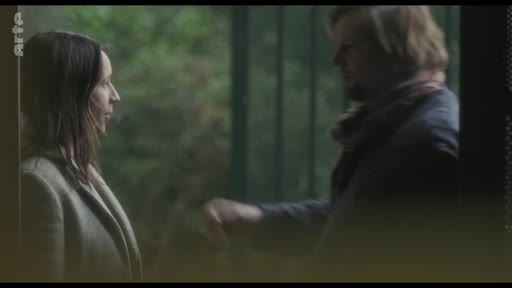 Un homme et une femme se tiennent face à face dans un cadre extérieur, engagés dans une conversation. La scène capture une interaction intime entre les deux personnages.