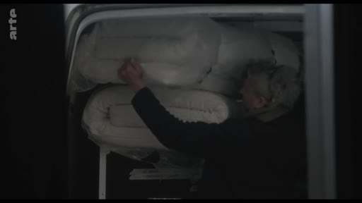 Une personne charge des matelas blancs dans l'arrière d'un véhicule, illustrant les préparatifs logistiques d'une installation ou d'un déménagement.