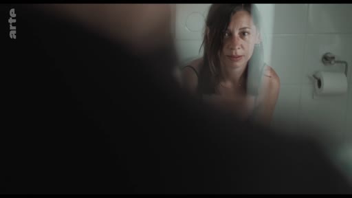 Une femme se regarde dans un miroir dans une salle de bain, illustrant une scène de réflexion personnelle ou de tension dans le cadre d'une relation.
