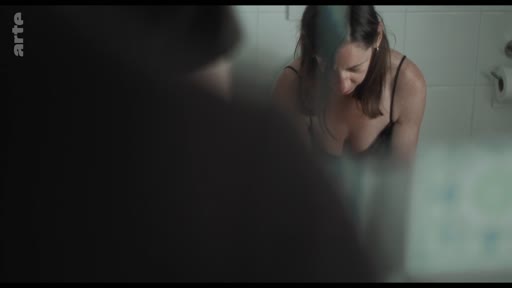 Une femme en tenue légère se regarde dans un miroir de salle de bain, dans une scène évoquant l'intimité et les réflexions sur une relation amoureuse.