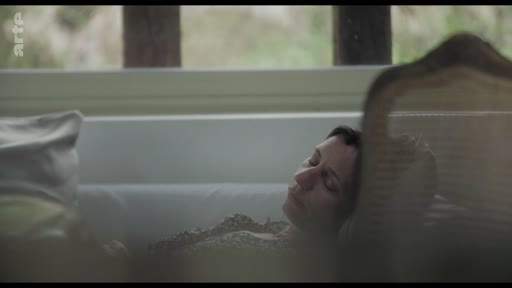 Une femme allongée dans une baignoire, les yeux fermés, dans une scène de contemplation et de repos. L'image capture un moment d'intimité et de calme.