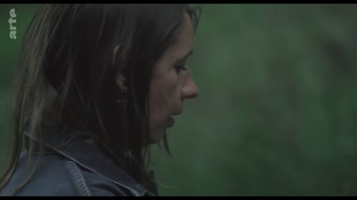 Gros plan sur le visage d'une femme de profil, filmée dans un environnement extérieur sombre et brumeux, évoquant une scène de fiction ou de documentaire.