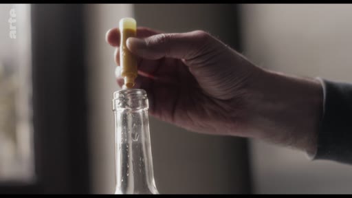 Gros plan sur une main en train de sceller une bouteille en verre avec un bouchon en cire, illustrant les étapes de préparation artisanale ou de conditionnement.