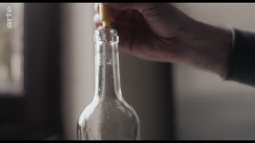 Une main insère un bouchon dans le goulot d'une bouteille en verre vide, illustrant une étape de préparation ou de conditionnement.