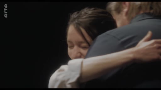 Un homme et une femme sont filmés en gros plan alors qu'ils s'enlacent, dans une scène intime et émotionnelle.