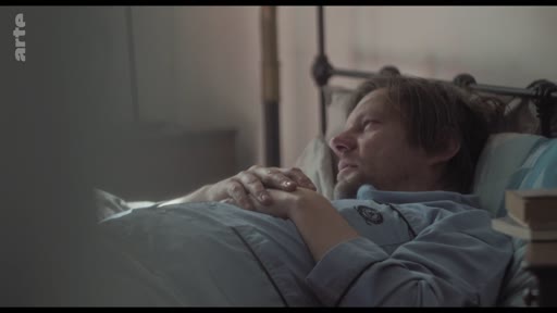 Un homme en pyjama est allongé dans un lit, semblant pensif ou préoccupé, dans une scène illustrant une période de convalescence ou de repos.