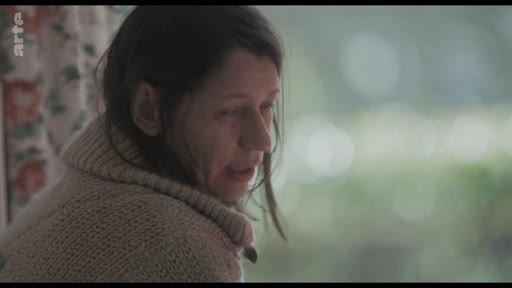 Une femme, vêtue d'un pull en laine à col roulé, est filmée en gros plan alors qu'elle semble discuter ou réfléchir, dans le cadre d'une séquence sur une blessure.