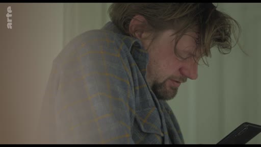 Un homme barbu, aux cheveux ébouriffés, consulte son smartphone avec une expression pensive ou inquiète, illustrant le thème de la communication isolée.