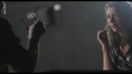 Une femme s'exprime lors d'une répétition ou d'une séance de travail artistique, filmée en plan moyen dans une ambiance tamisée.