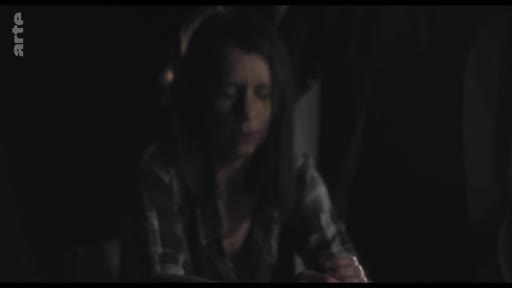 Une femme au visage partiellement éclairé dans une scène sombre, capturée lors d'un moment intense de tournage.