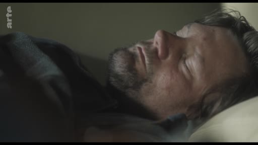 Un homme barbu est allongé et dort dans un lit, capturé dans un moment de repos ou de solitude.