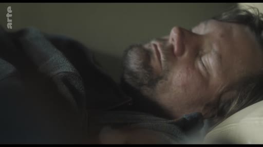 Un homme barbu est allongé et dort dans un lit, capturé dans un moment de repos ou de réflexion solitaire.