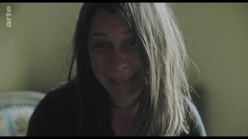 Une femme, filmée en gros plan, semble émue ou en train de se confier lors d'une séquence d'entretien. L'expression de son visage suggère un moment de vulnérabilité ou une confession personnelle.