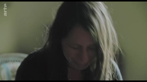Une femme, filmée en gros plan, semble traverser un moment d'émotion profonde ou de confession personnelle, le visage incliné vers le bas.