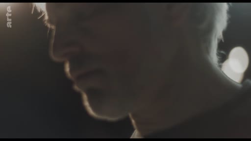 Gros plan sur le visage d'un homme dans une séquence à l'éclairage tamisé, illustrant un moment de réflexion ou de confidence.