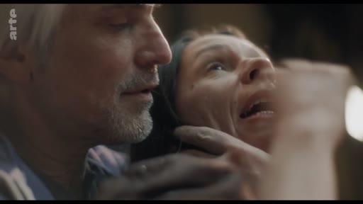 Un homme aux cheveux gris saisit le visage d'une femme qui semble effrayée ou en détresse lors d'une scène de fiction dramatique. Cette séquence illustre une discussion sur les techniques de jeu d'acteur.