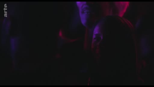 Une femme est visible dans une foule lors d'un concert, éclairée par des lumières de scène violettes et rouges, illustrant l'intensité émotionnelle d'une performance musicale.