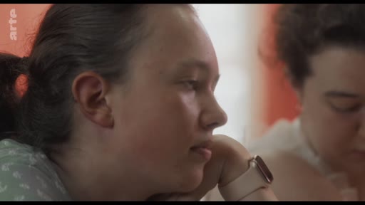 Une jeune femme est filmée en gros plan lors d'un atelier de réflexion, exprimant une attitude pensive et attentive.