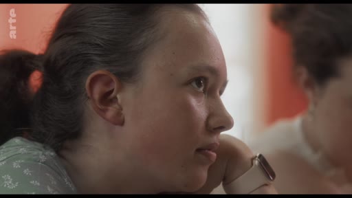 Une jeune femme attentive participe à un atelier de réflexion, portant une montre connectée au poignet. Elle semble écouter activement lors d'une session de travail en groupe.