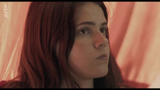 Une jeune femme aux cheveux roux est filmée en gros plan lors d'une discussion en classe portant sur le thème des traumatismes. Elle semble concentrée et pensive, illustrant une séquence de témoignage ou de réflexion collective.