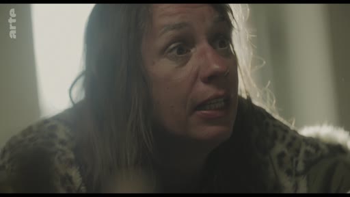 Une femme au visage marqué par l'émotion et la tension, filmée en gros plan, semble être au cœur d'une dispute ou d'une confrontation dramatique.