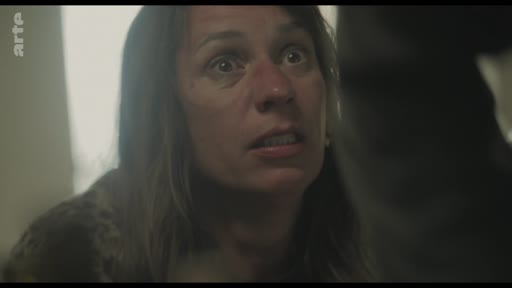 Gros plan sur le visage d'une femme exprimant de la peur ou une vive inquiétude au cours d'une scène de dispute domestique. L'expression faciale intense souligne la tension dramatique de la séquence.
