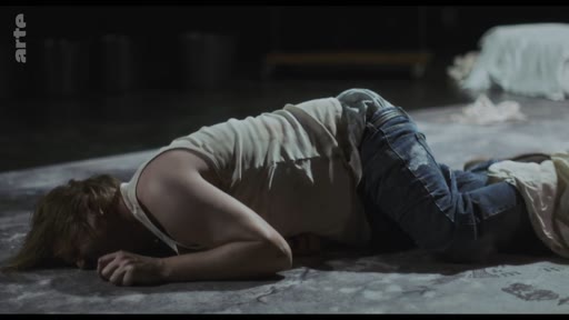 Un acteur en débardeur et jean est allongé sur le sol dans une posture dramatique lors d'une représentation théâtrale captée par la chaîne Arte.